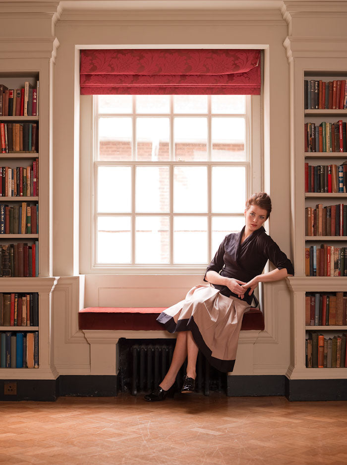 Woman sitting on a window sill in a library with bookshelves on either side.